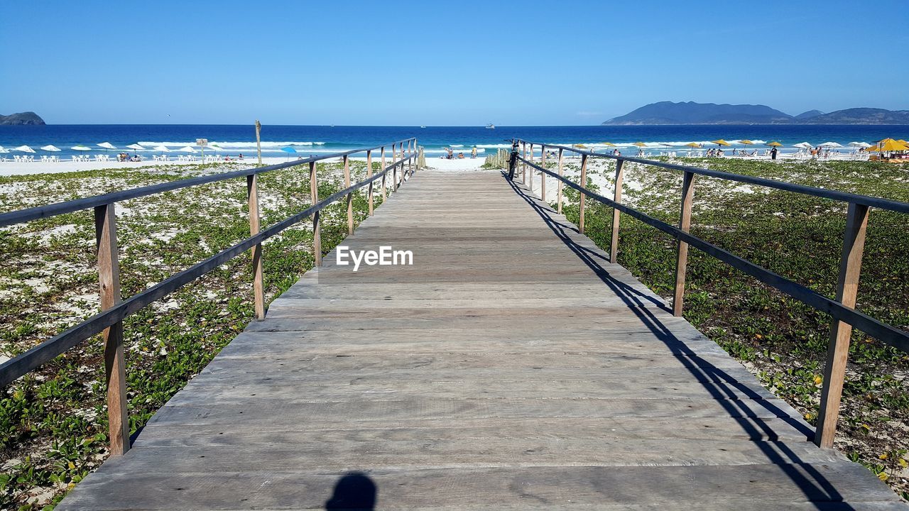 Boardwalk leading towards sea against clear sky