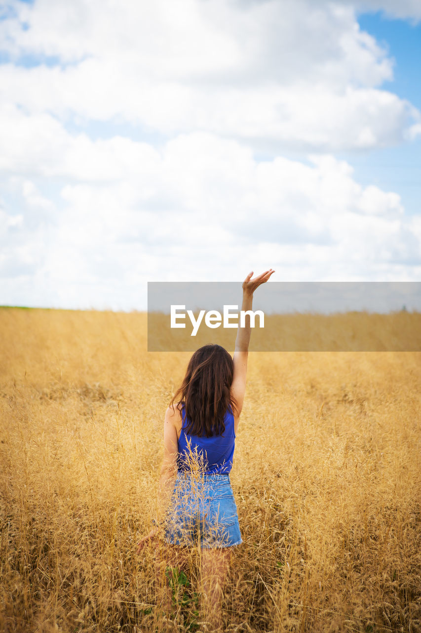 A girl in a blue t-shirt and denim shorts stands in the middle of a field