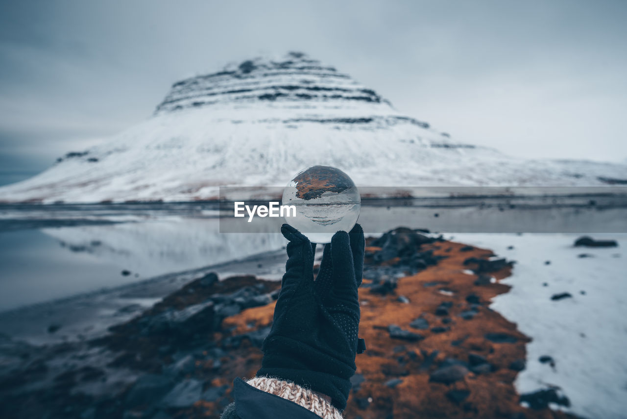 Cropped hand holding crystal ball with reflection by lake