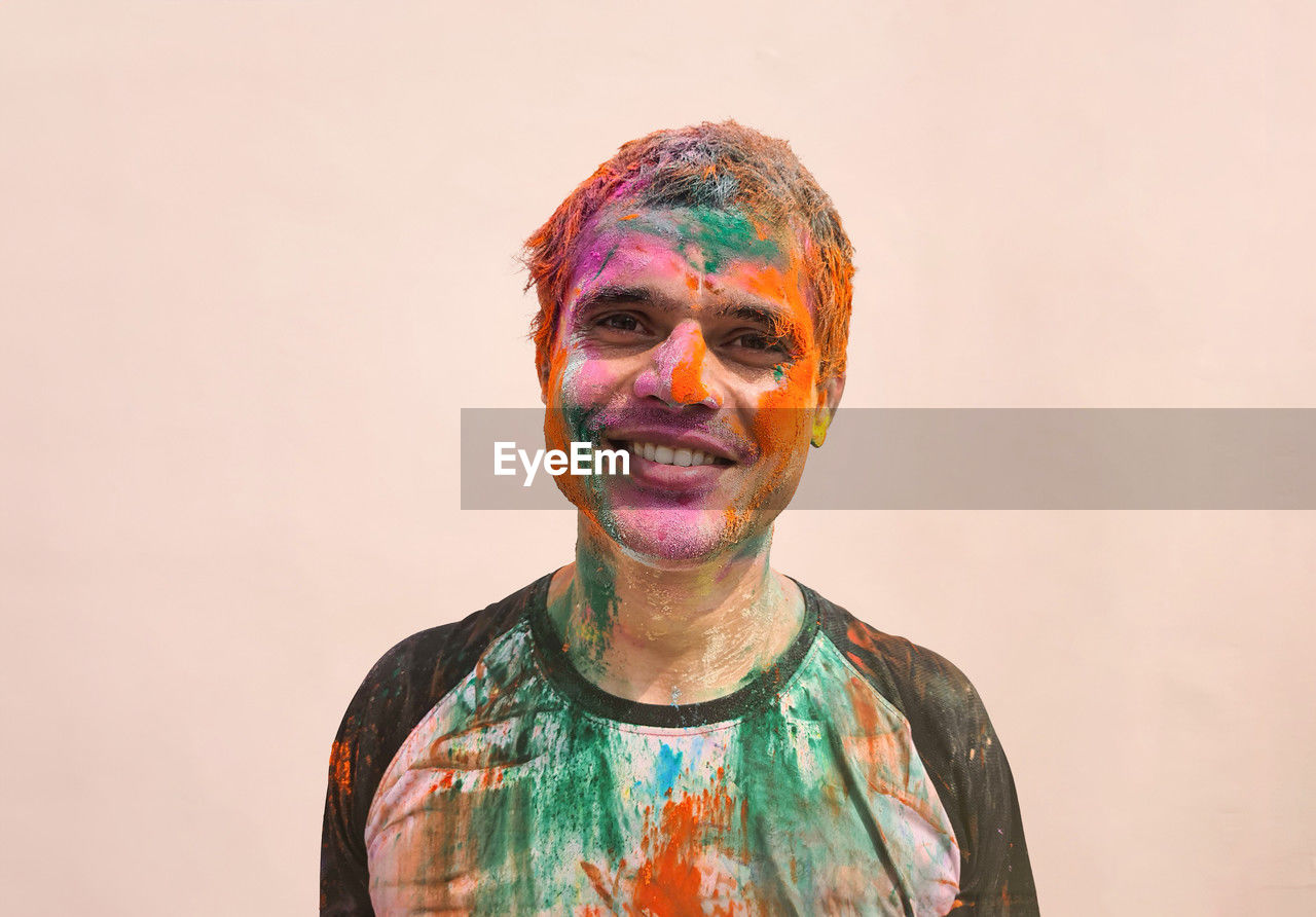 Portrait of indian man covered in holi colors against plain background 