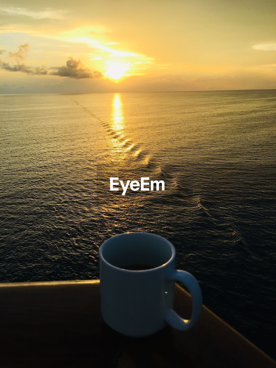 COFFEE CUP AND SEA AGAINST SKY DURING SUNSET