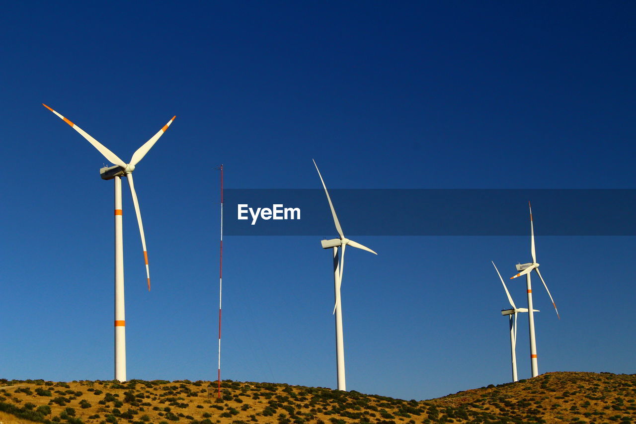 Low angle view of wind turbines on field against clear sky