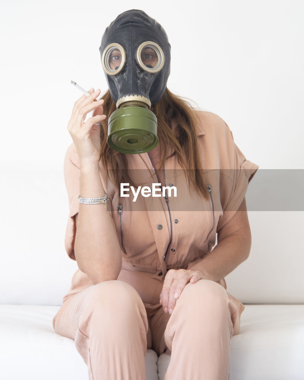 Portrait of woman wearing gas mask holding cigarette against wall
