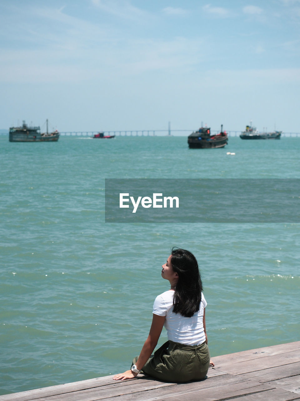 Woman sitting on pier over sea against sky