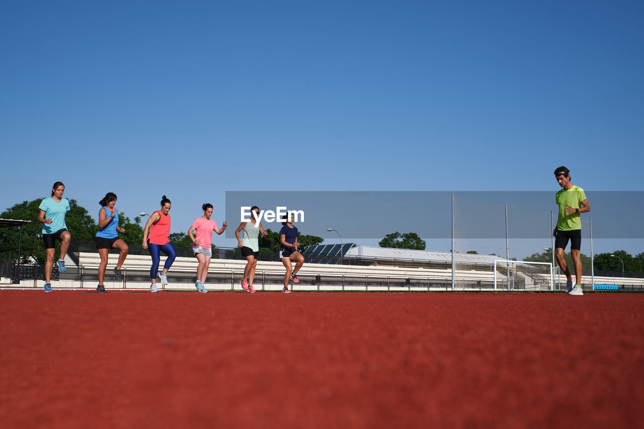 Group of women practice pre-workout stretching with their young traine