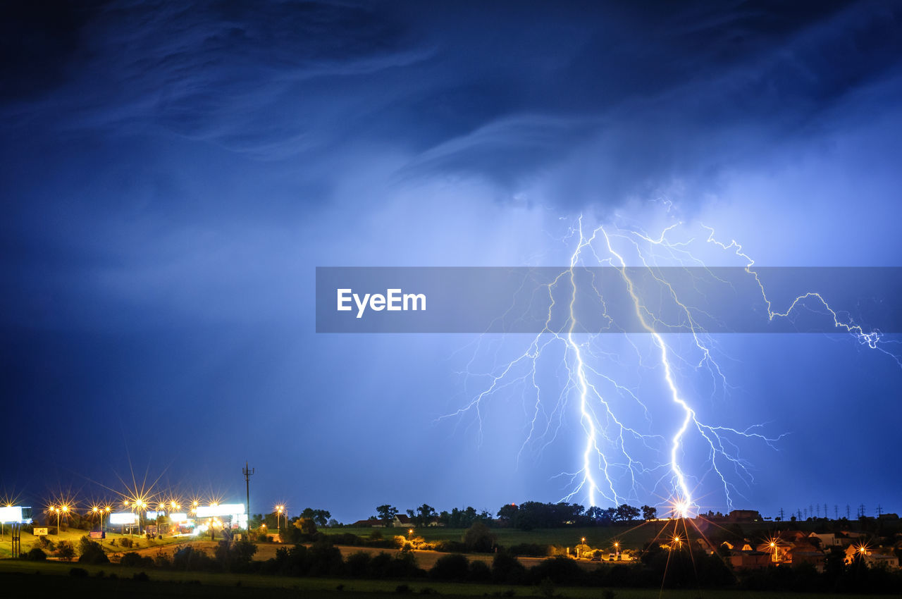 LIGHTNING OVER ILLUMINATED BUILDINGS AGAINST SKY