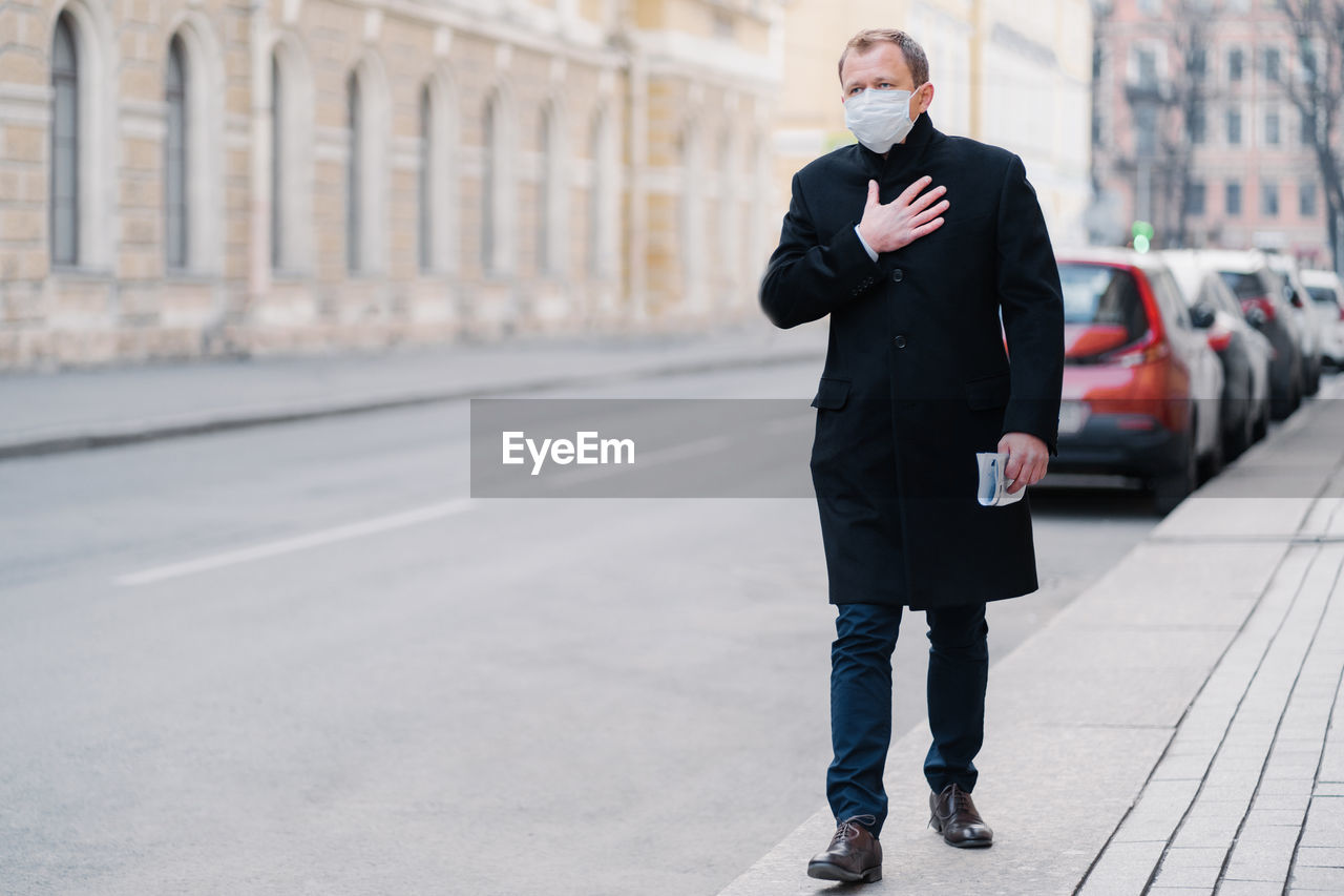 Full length of man wearing mask walking on sidewalk in city