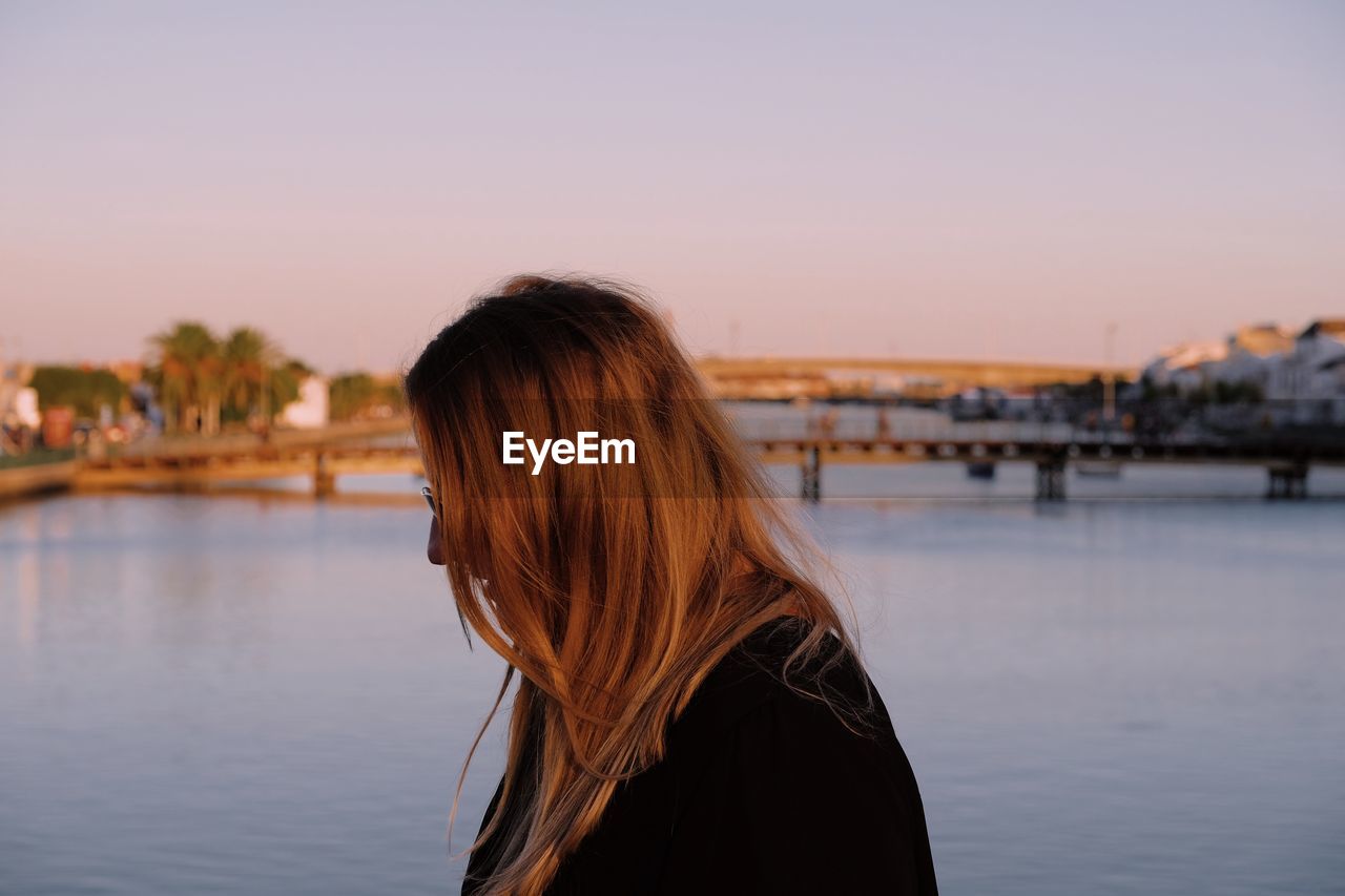 Side view of woman standing against river during sunset