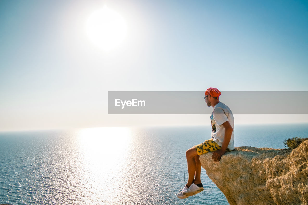 Man sitting on rock over sea against sky