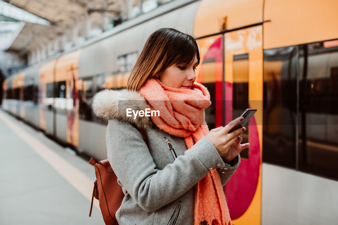 Woman using mobile phone while standing at railroad station platform