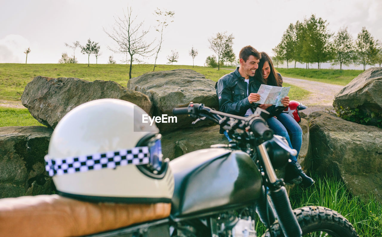 Young couple sitting looking at a map during a trip with motorcycle in foreground