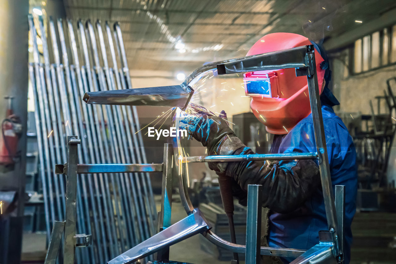 Welder in production is engaged in the manufacture of products. in a mask, in gloves, sparks fly
