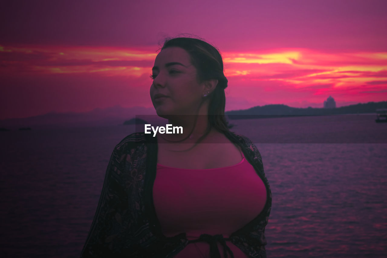 Young woman looking at sea against sky during sunset