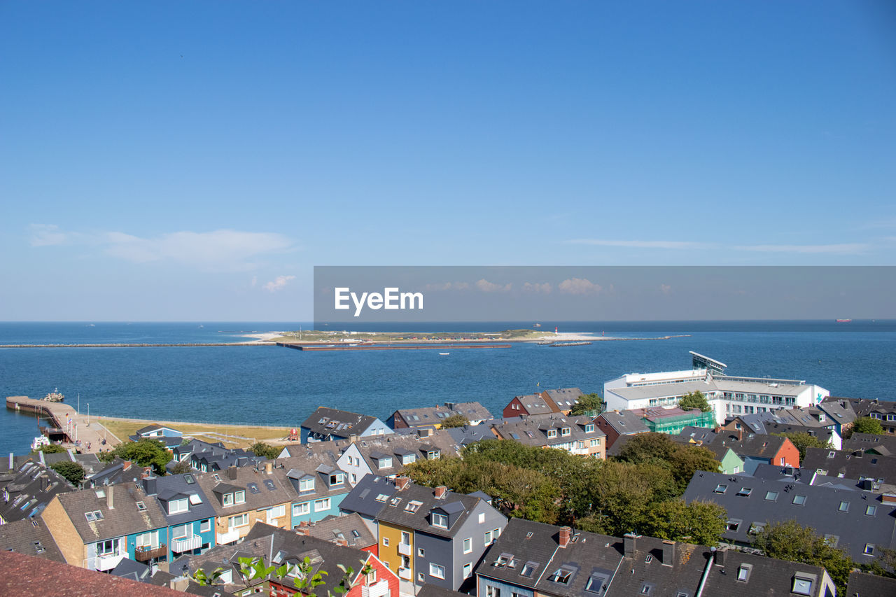 HIGH ANGLE VIEW OF BUILDINGS BY SEA AGAINST BLUE SKY