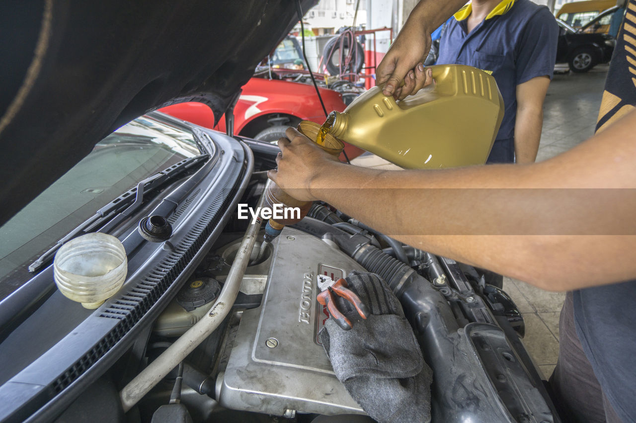 Midsection of mechanic pouring oil in container 