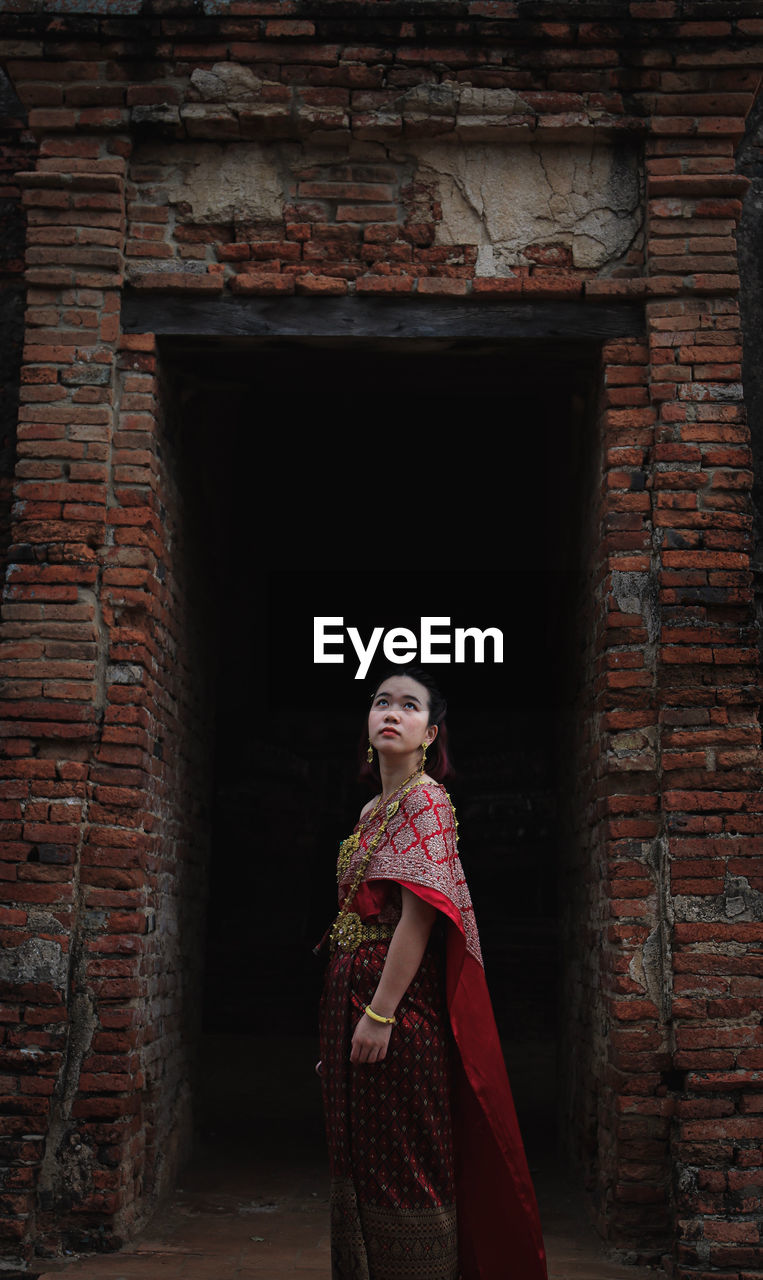 Side view of woman standing in traditional clothing against brick wall