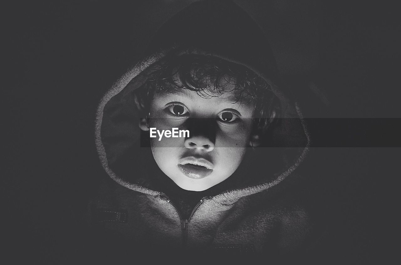 Close-up portrait of cute boy wearing hooded jacket in darkroom