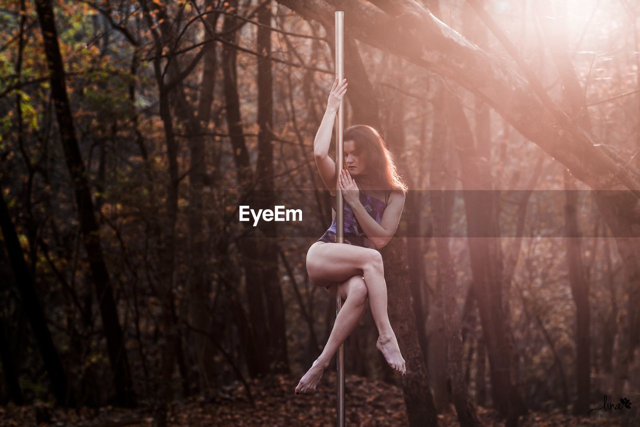 Woman dancing on pole against trees in forest