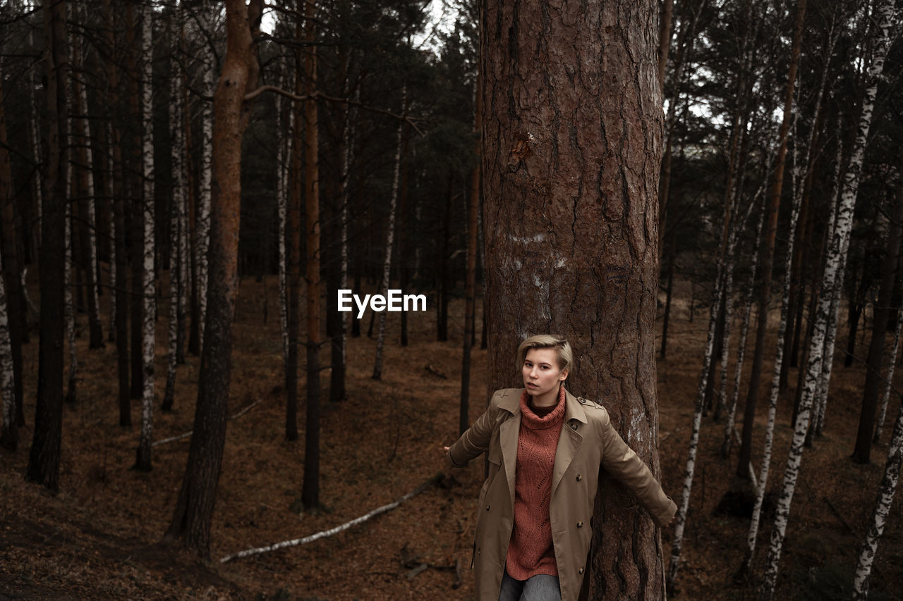 Portrait of woman standing by tree trunk in forest