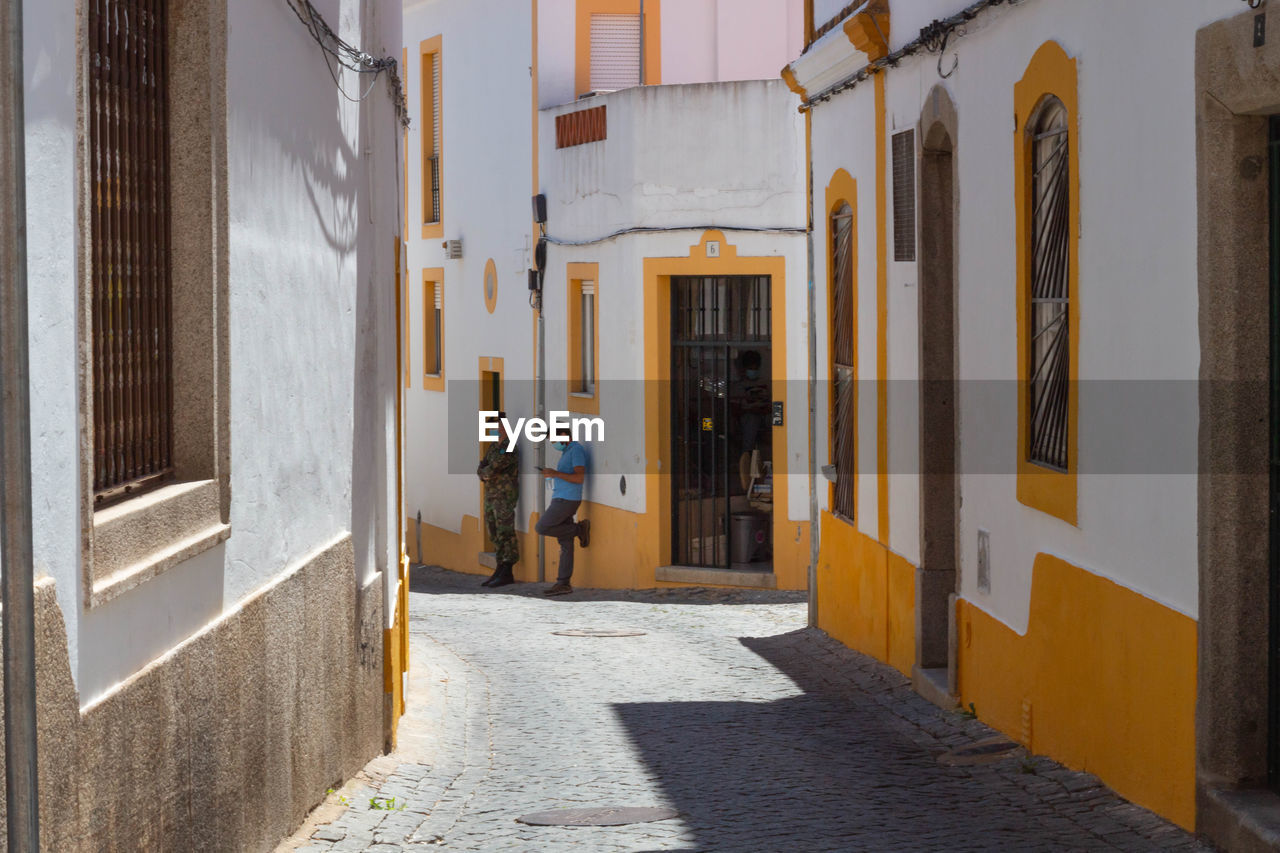 REAR VIEW OF PEOPLE WALKING IN ALLEY AMIDST BUILDINGS