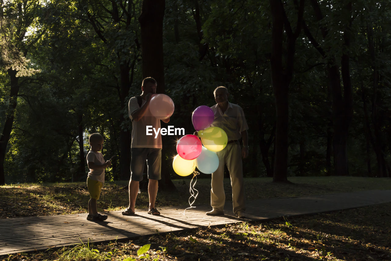 Grandfather, dad and son, the whole family spend time in the park and inflate balloons.