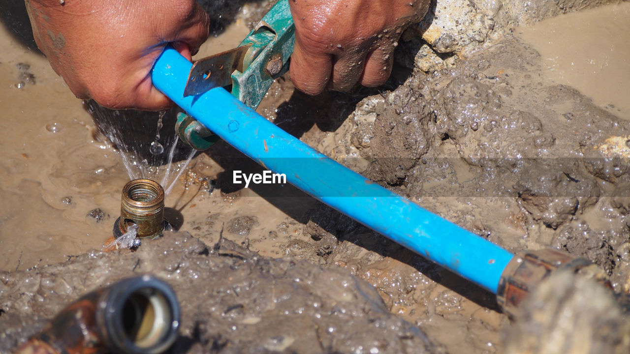 Cropped hands of man repairing pipe in mud