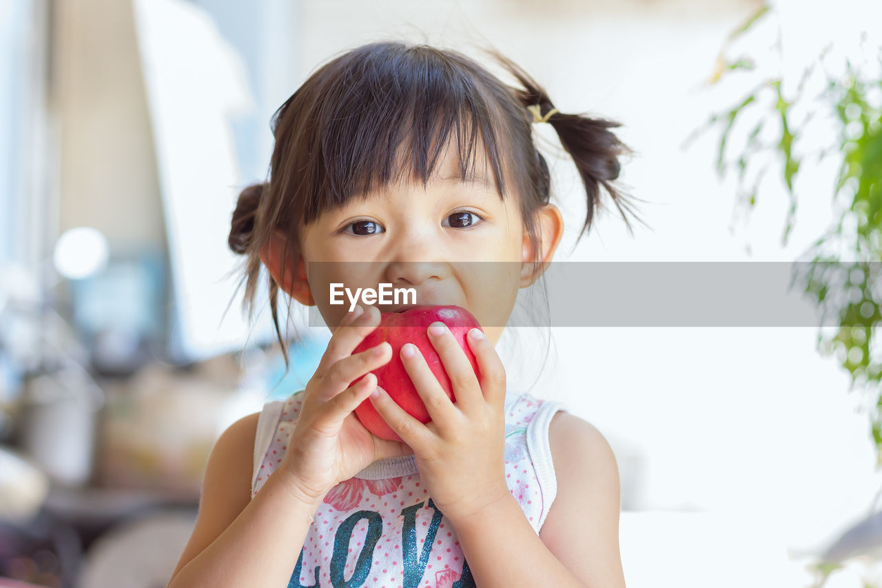 Close-up portrait of girl eating apple at home