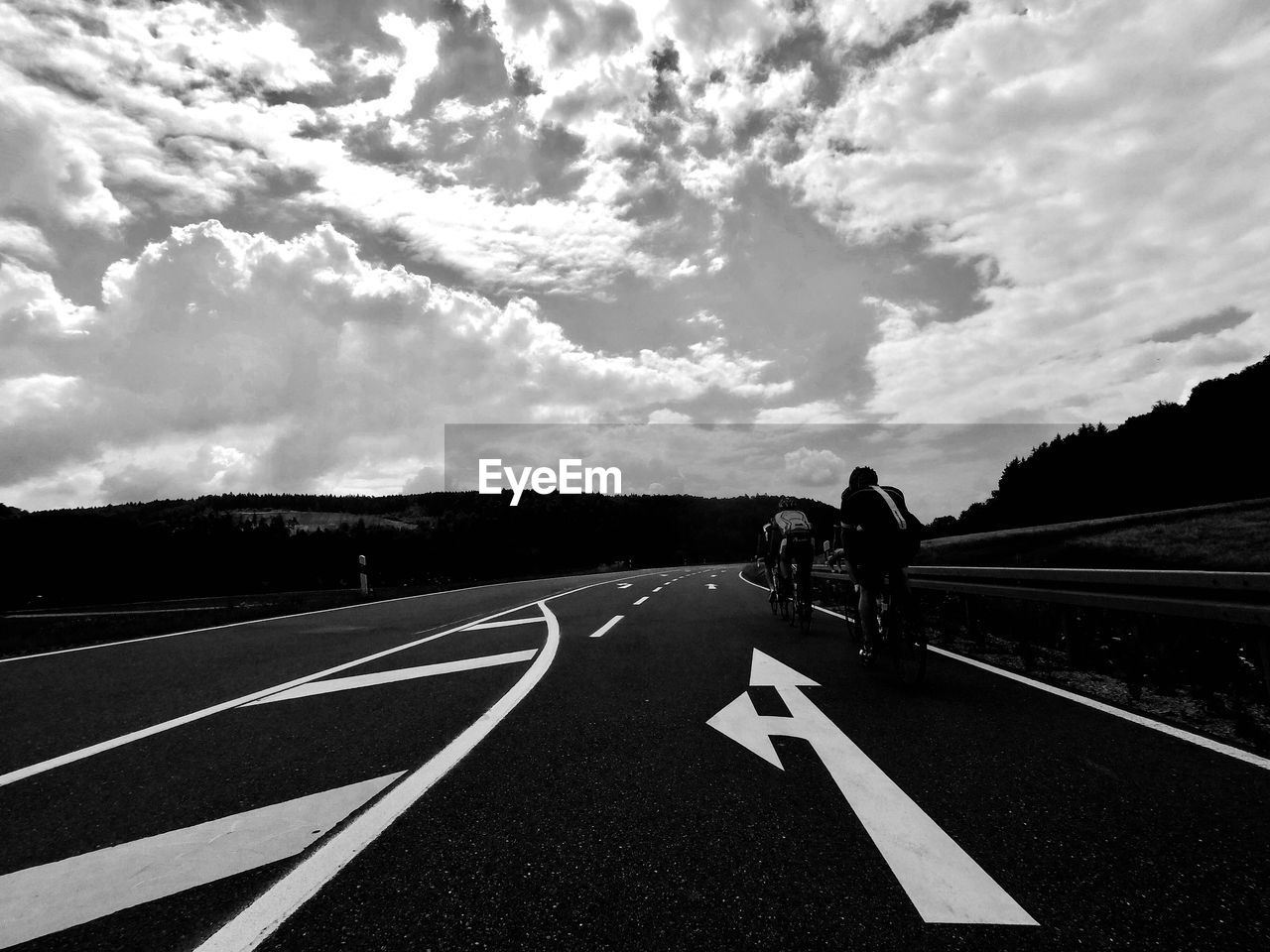 Men riding motorcycle on road against cloudy sky