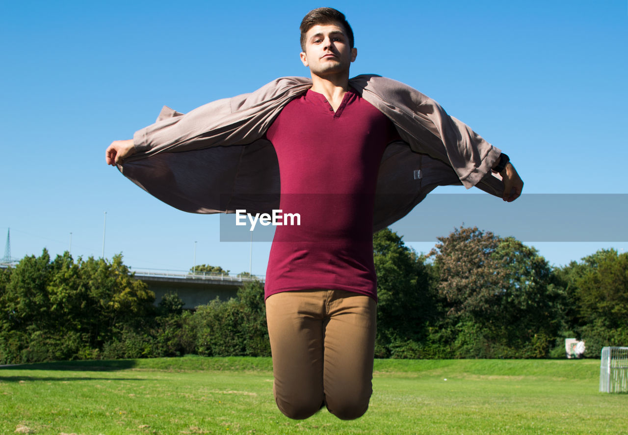 Portrait of man wearing jacket and jumping on grassy field at park