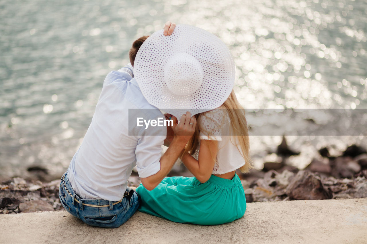 Couple with hat romancing on retaining wall by sea