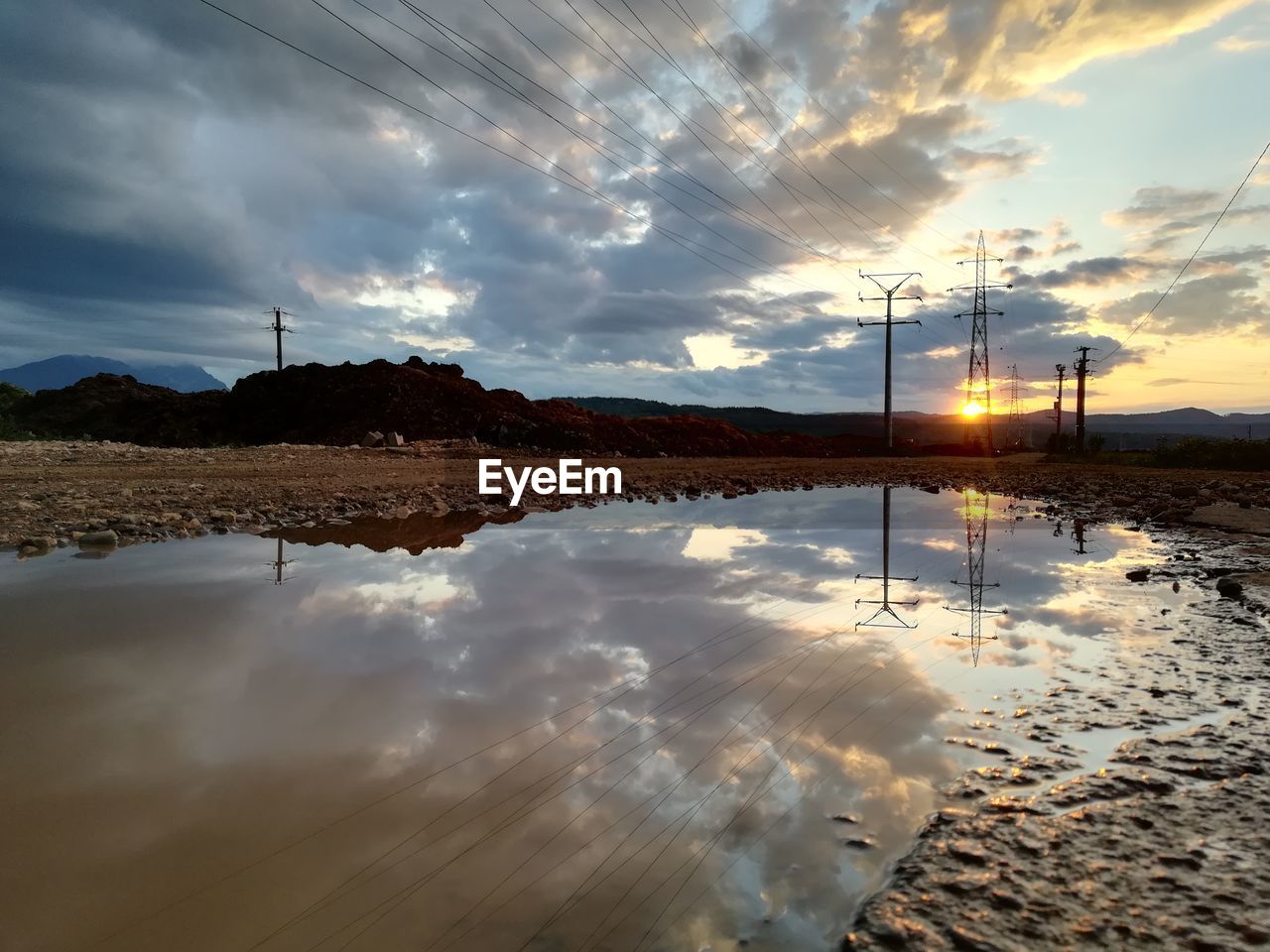 REFLECTION OF ELECTRICITY PYLON ON LAND AGAINST SKY DURING SUNSET