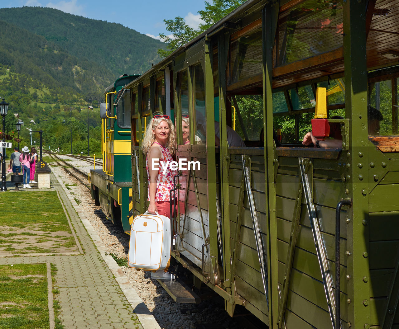 Woman holding a suitcase and getting on a vintage train - sarganska osmica