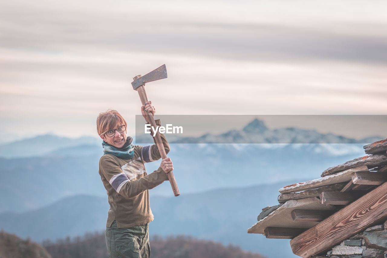 Portrait of angry woman holding axe against sky