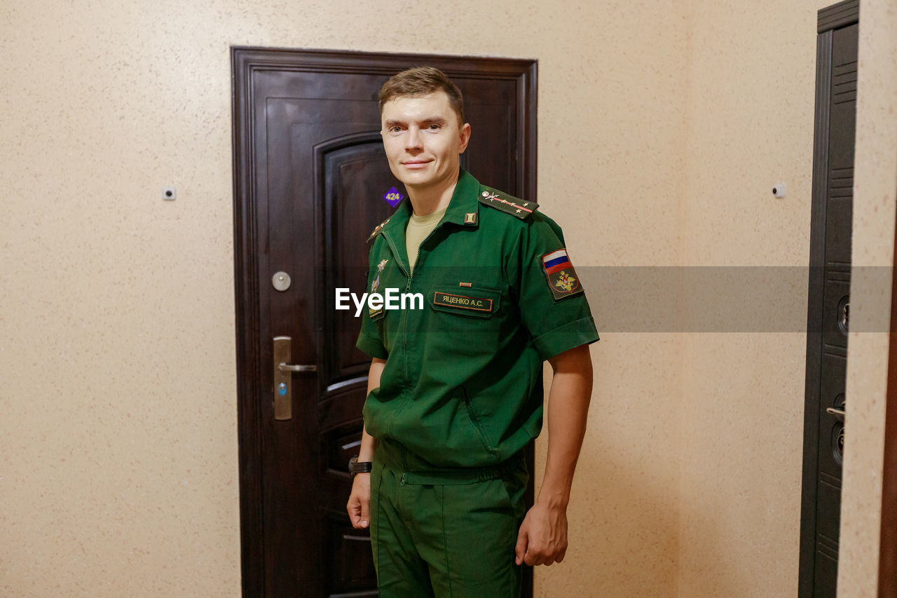 Portrait of man in uniform standing against door