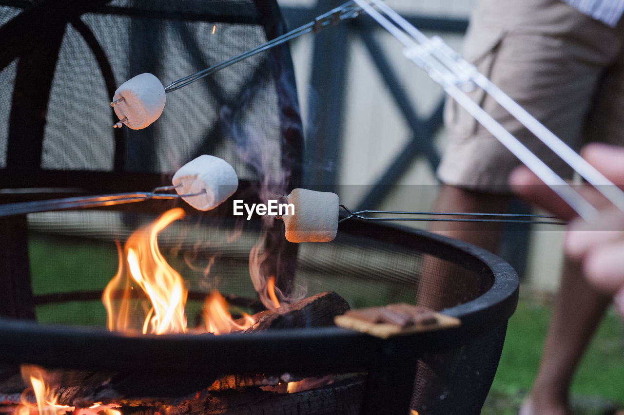 Midsection of man roasting marshmallow on campfire at yard