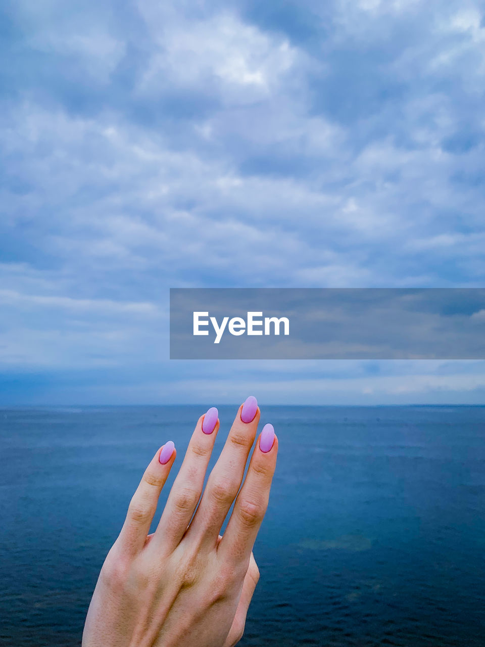 Woman hand by sea against sky