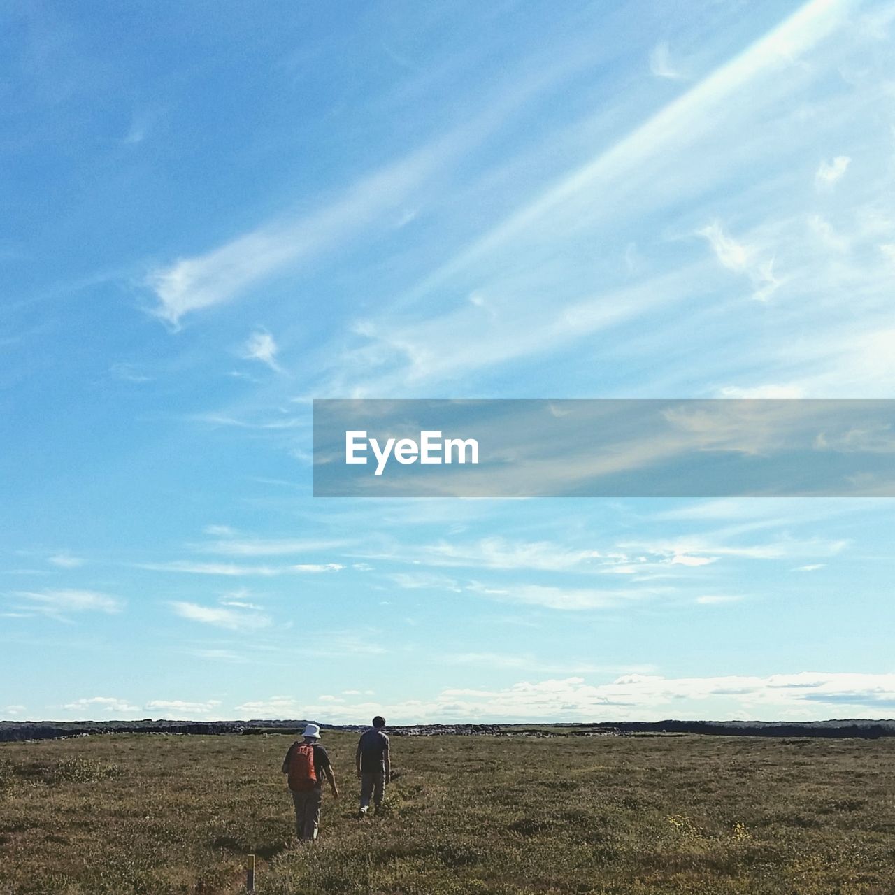 REAR VIEW OF MEN STANDING AT BEACH AGAINST SKY