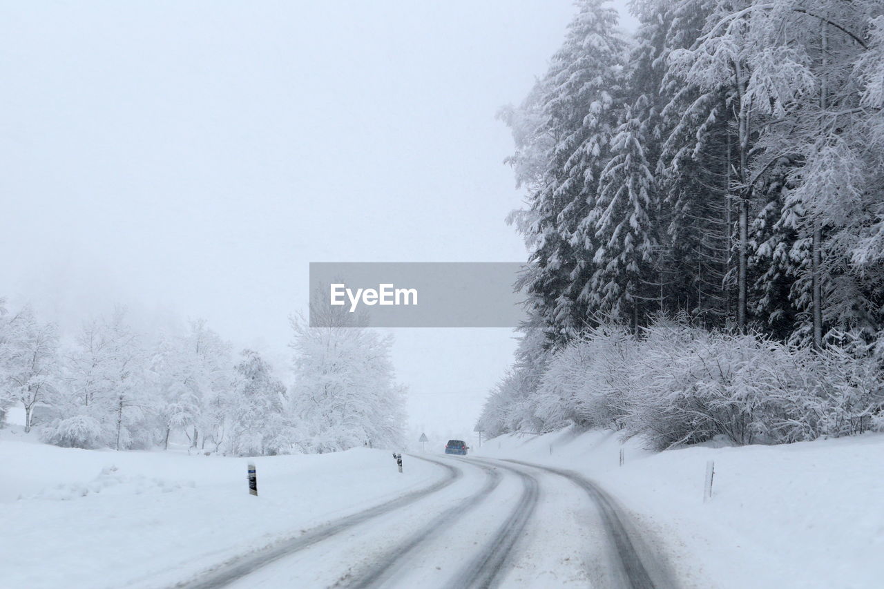 SNOW COVERED ROAD AMIDST TREES DURING WINTER