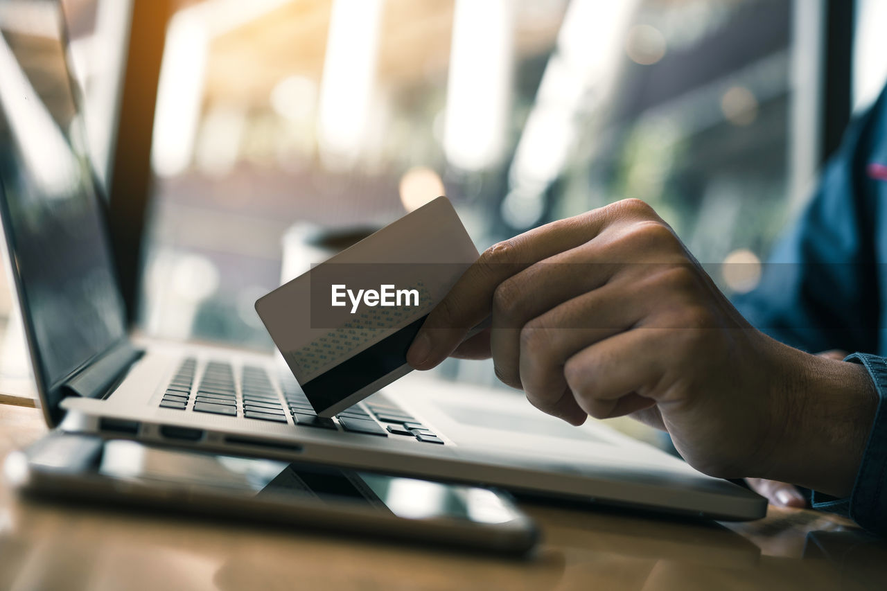 Cropped image of man holding credit card on laptop