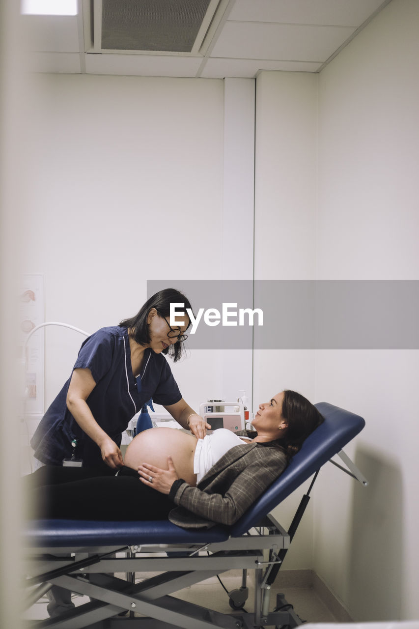 Female healthcare expert measuring abdomen of pregnant woman lying on gurney in medical clinic