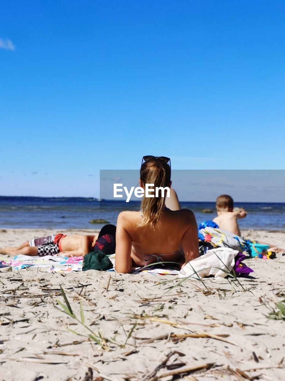 Rear view of mother with kids relaxing on beach against sky