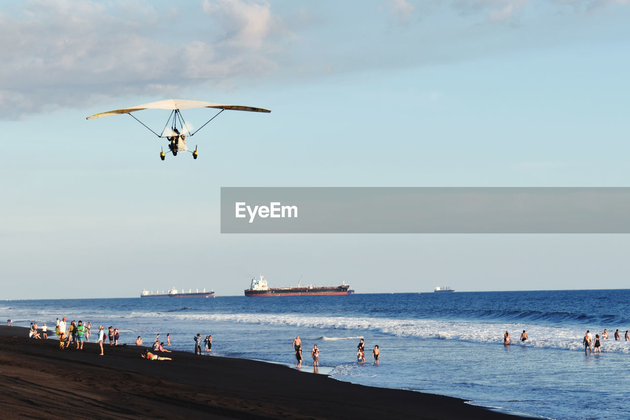 People enjoying at beach against sky, a plane and boats