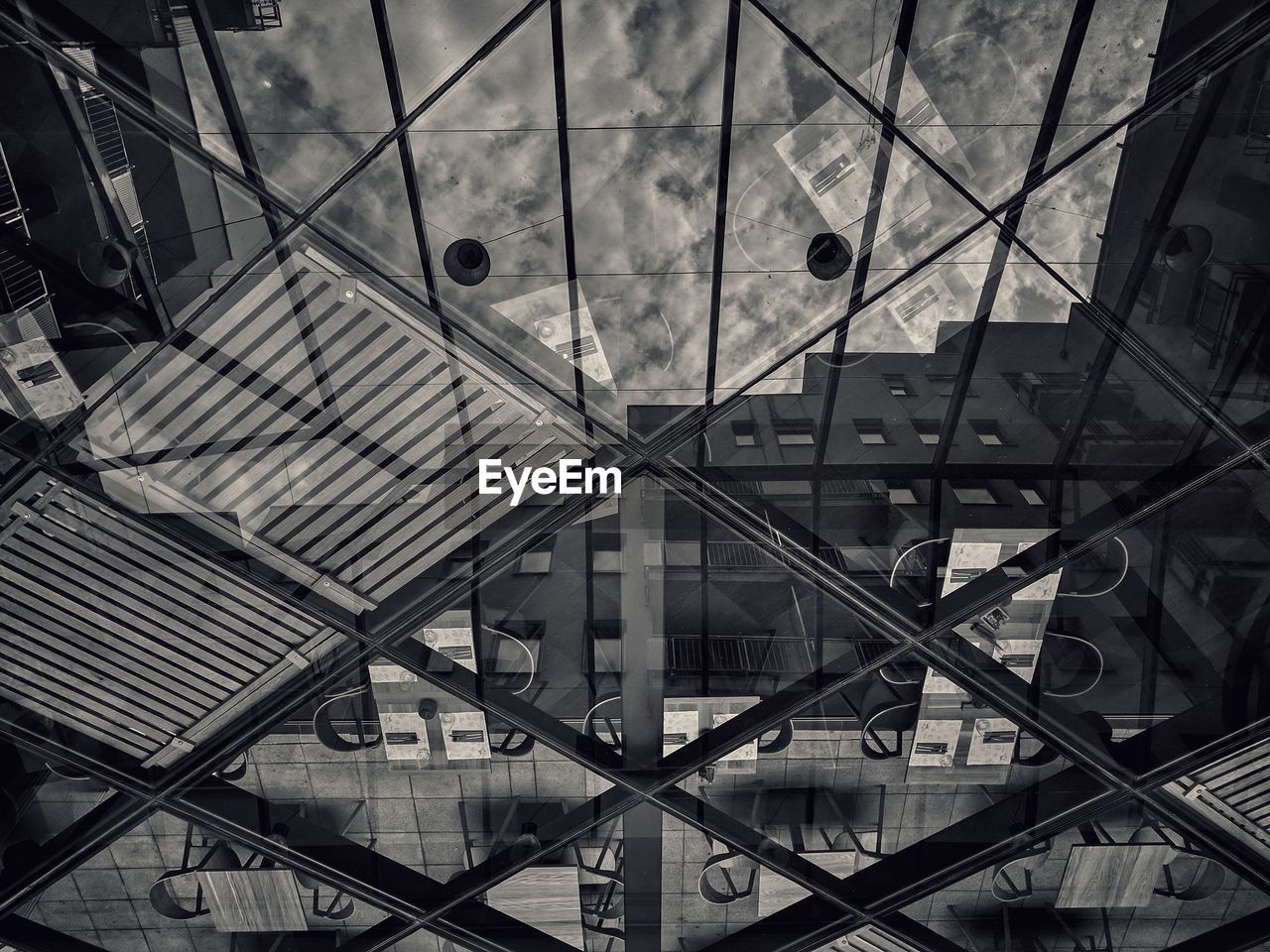 Tables an chairs in cafe seen through glass ceiling with reflection of building and sky