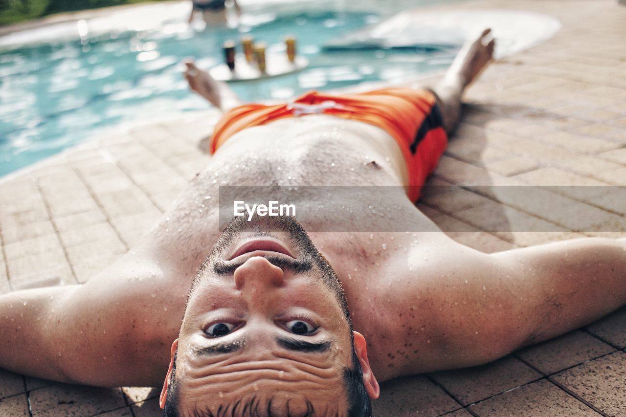 Portrait of shirtless man lying down by swimming pool