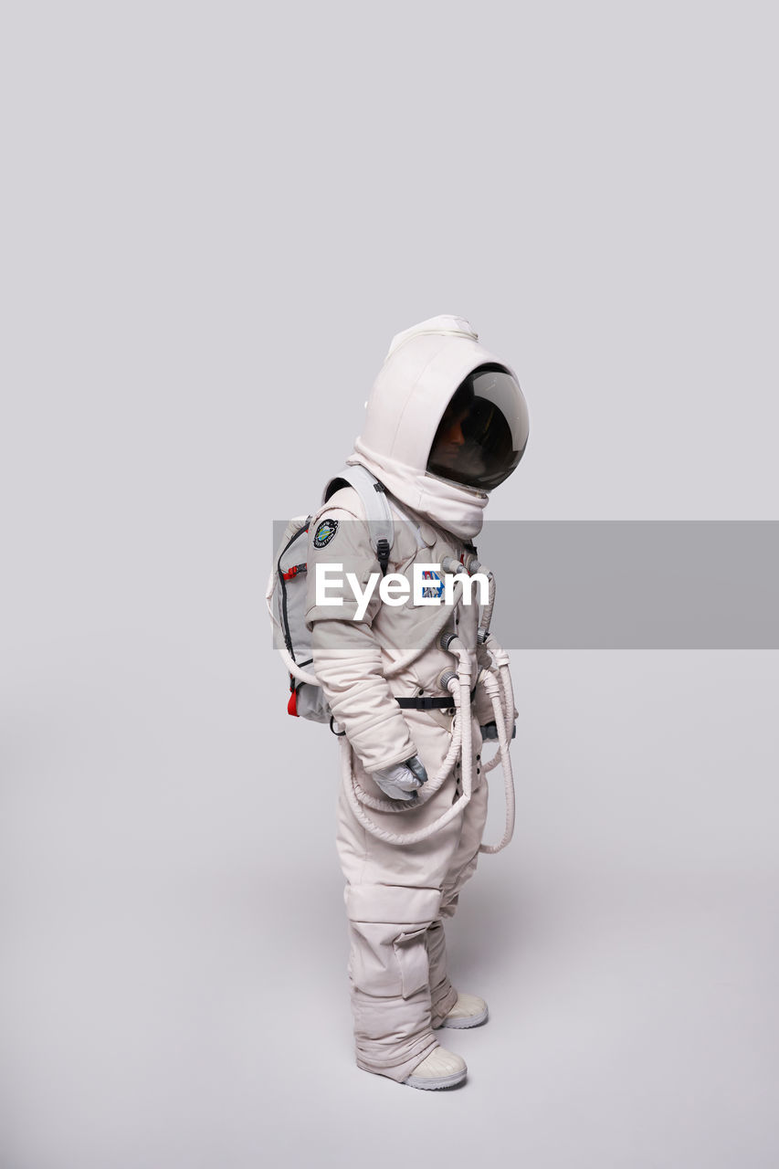 Full body side view of unrecognizable cosmonaut wearing protective helmet and spacesuit for exploring space in studio against white background