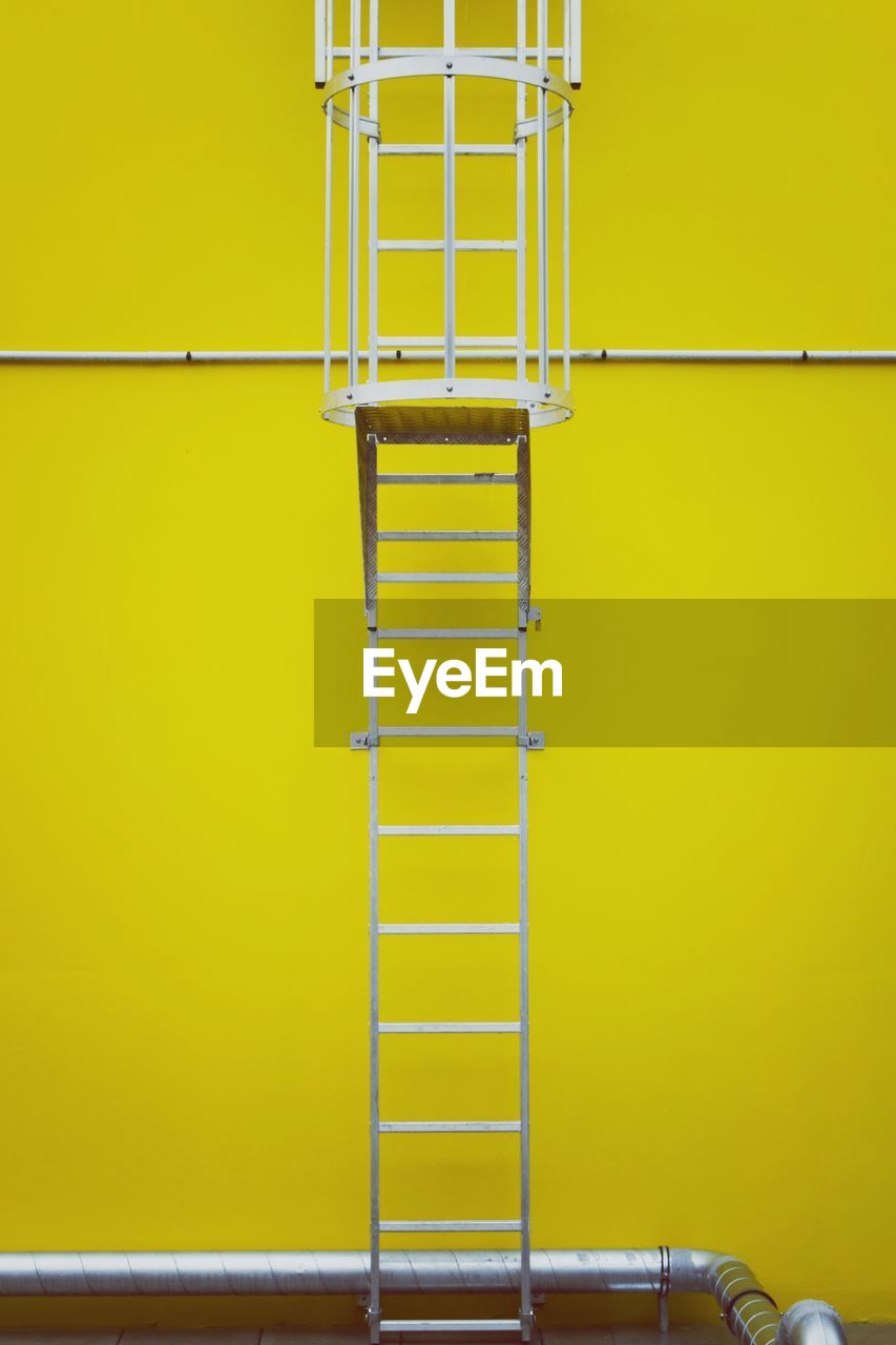 Metallic ladder against yellow wall