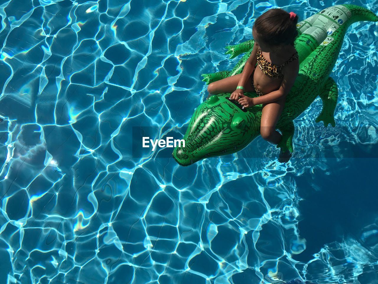 High angle view of girl sitting on inflatable crocodile in swimming pool