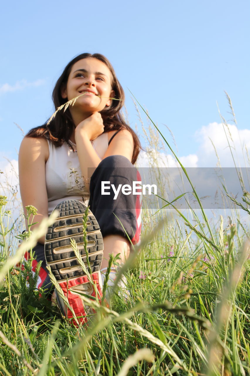 Smiling young woman standing on field against sky