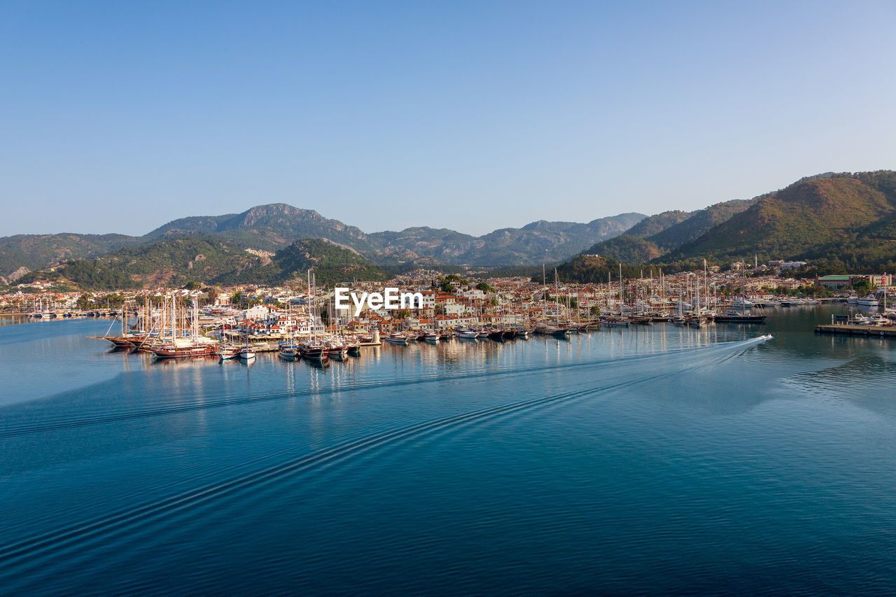 Sailboats in city by sea against clear blue sky