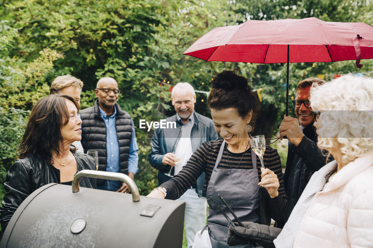 Smiling female friends cooking dinner on barbecue grill during party while it rains